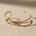 Brazalete NUDO dorado con nudo central sobre lino beige